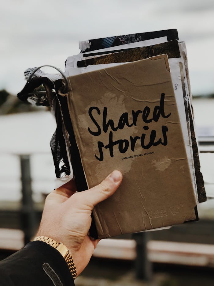 our-story Hand holds a u0022Shared Storiesu0022 journal against a blurred outdoor backdrop, emphasizing creativity and personal storytelling.